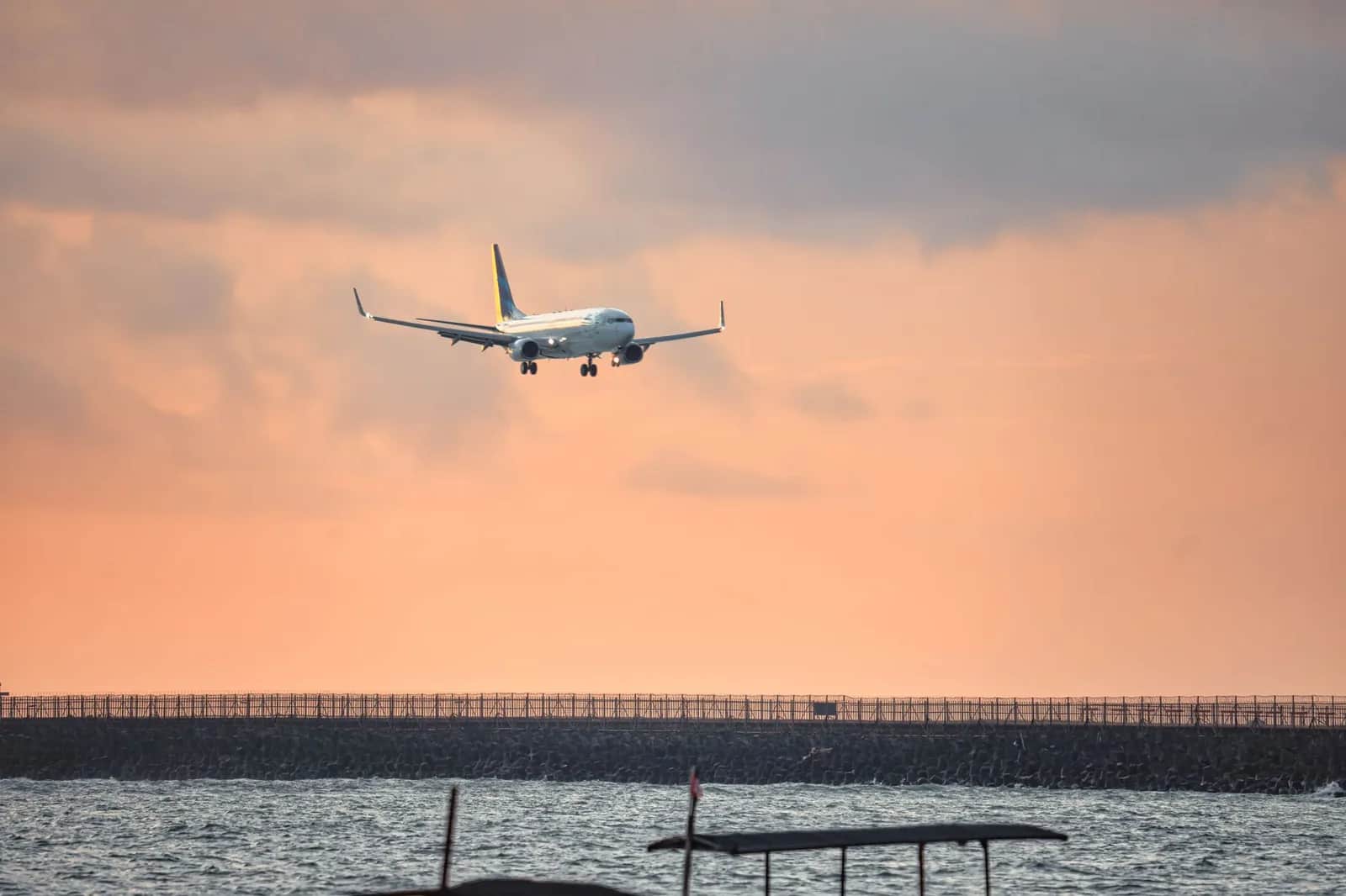 Avion en approche au-dessus de la mer, près de la piste de l'aéroport Ngurah Rai à Bali, au coucher du soleil