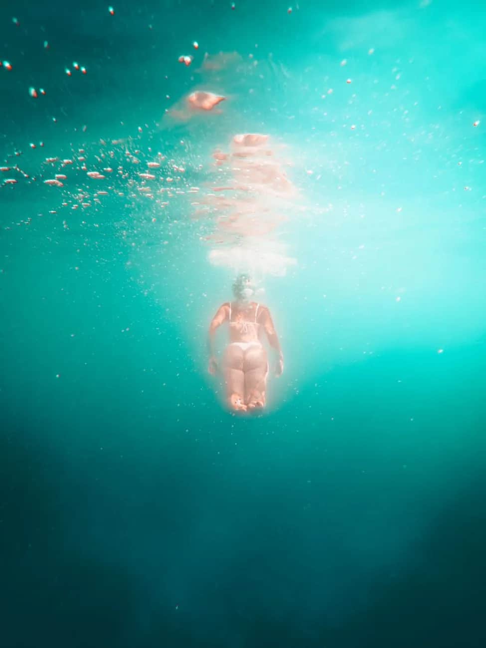 Apnéiste en descente sous la surface dans une eau turquoise limpide, chapelet de bulles, Amed, Bali