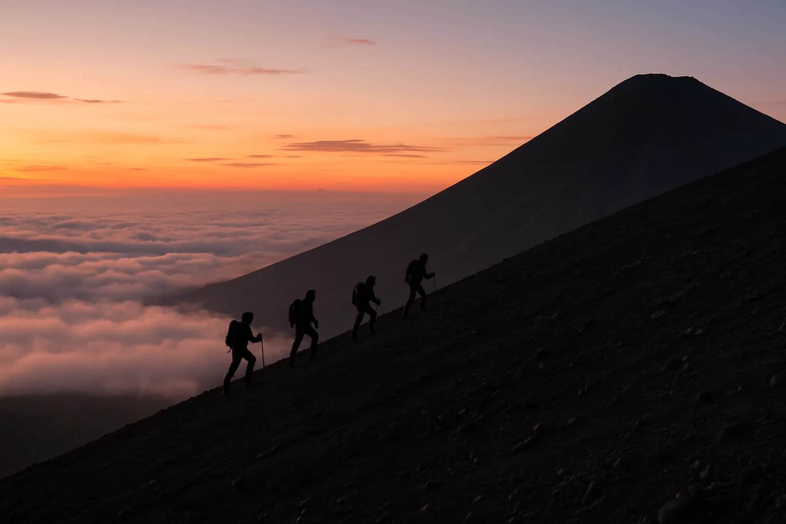 Randonneurs en file sur la pente cendreuse d'un volcan conique au-dessus d'une mer de nuages au lever du jour, Bali