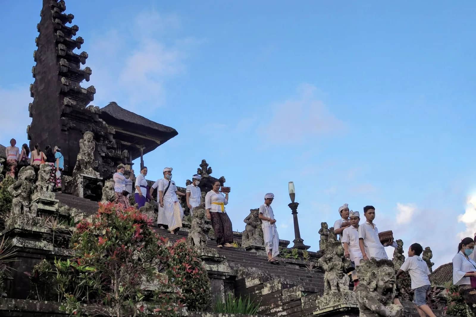 Fidèles balinais en tenue blanche descendant les escaliers de pierre du temple de Besakih entre les portes fendues, Bali