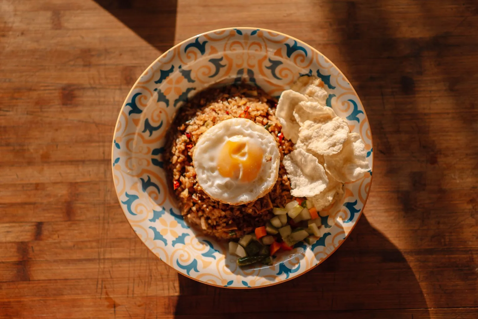 Nasi goreng indonésien avec œuf au plat et krupuk dans une assiette à motifs