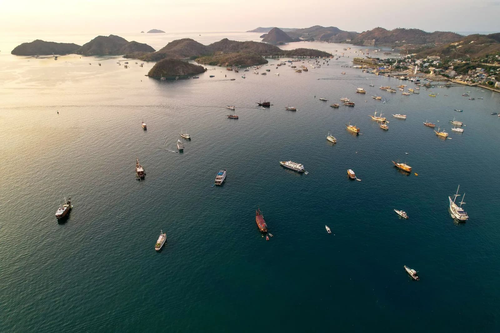 Vue aérienne de la baie de Labuan Bajo au coucher du soleil, avec des dizaines de phinisi au mouillage devant la ville, Florès