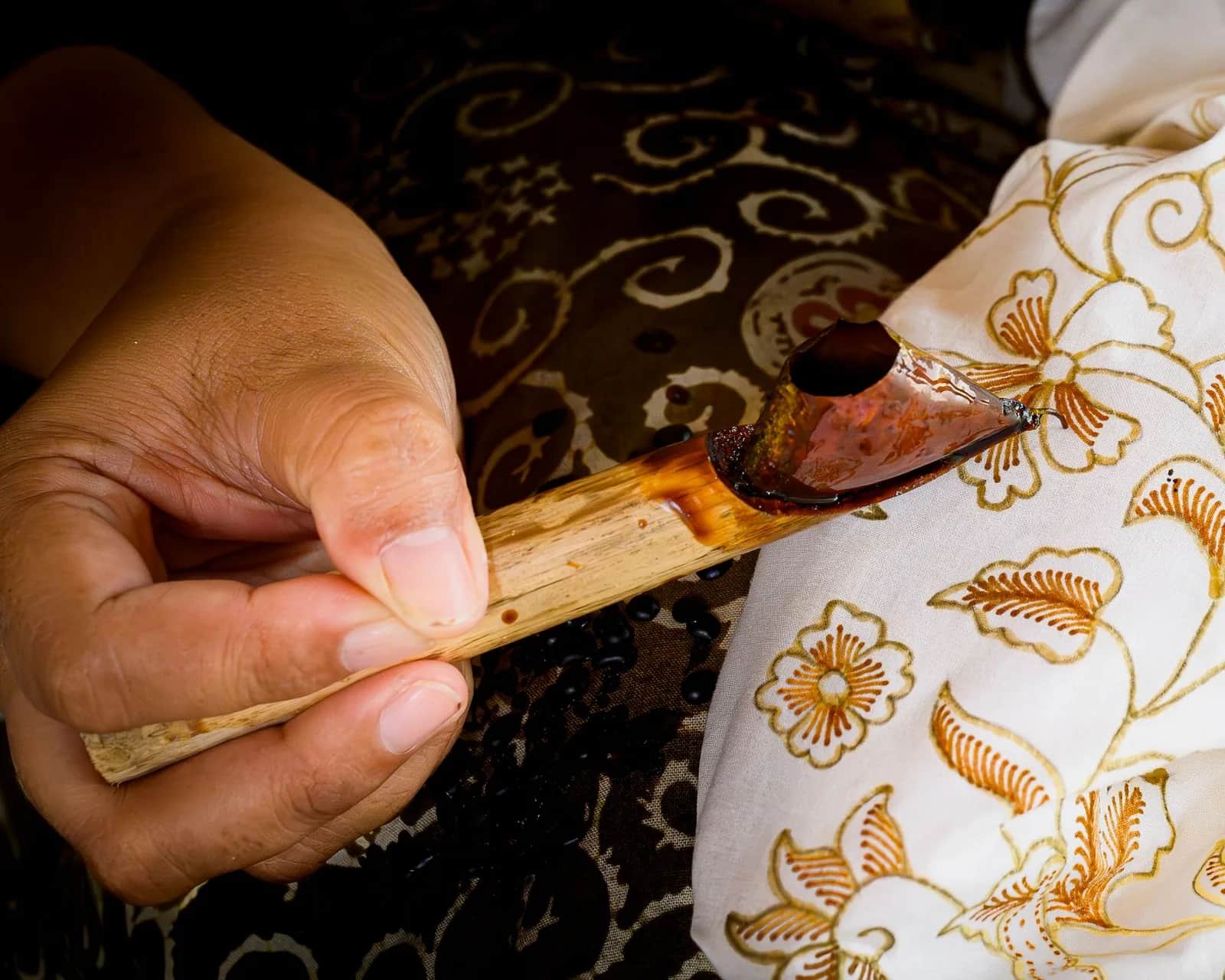 Main appliquant de la cire avec un canting sur un tissu batik