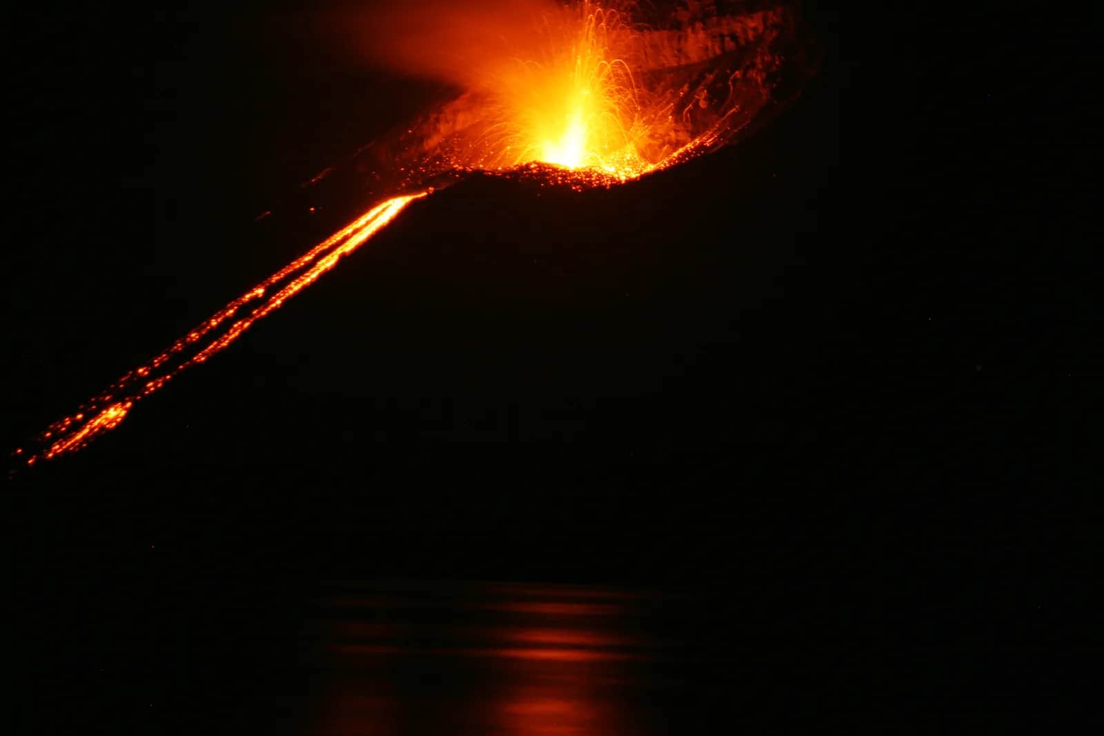 Éruption nocturne de l'Anak Krakatau : fontaine de lave et coulée incandescente se reflétant sur la mer, détroit de la Sonde