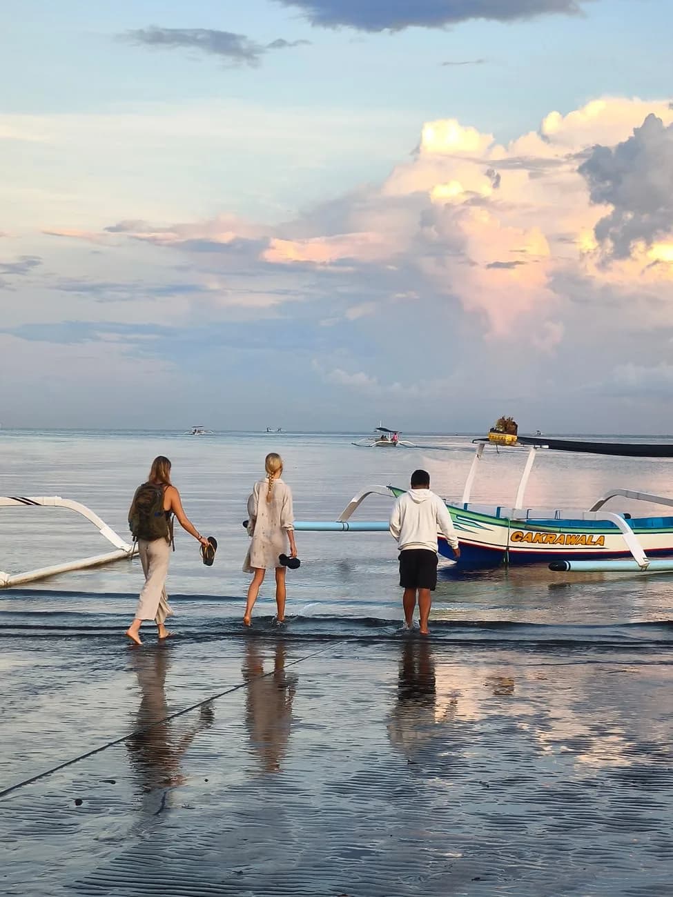 Voyageurs s'apprêtant à embarquer sur un jukung à balancier sur le sable mouillé au lever du jour à Lovina, Bali