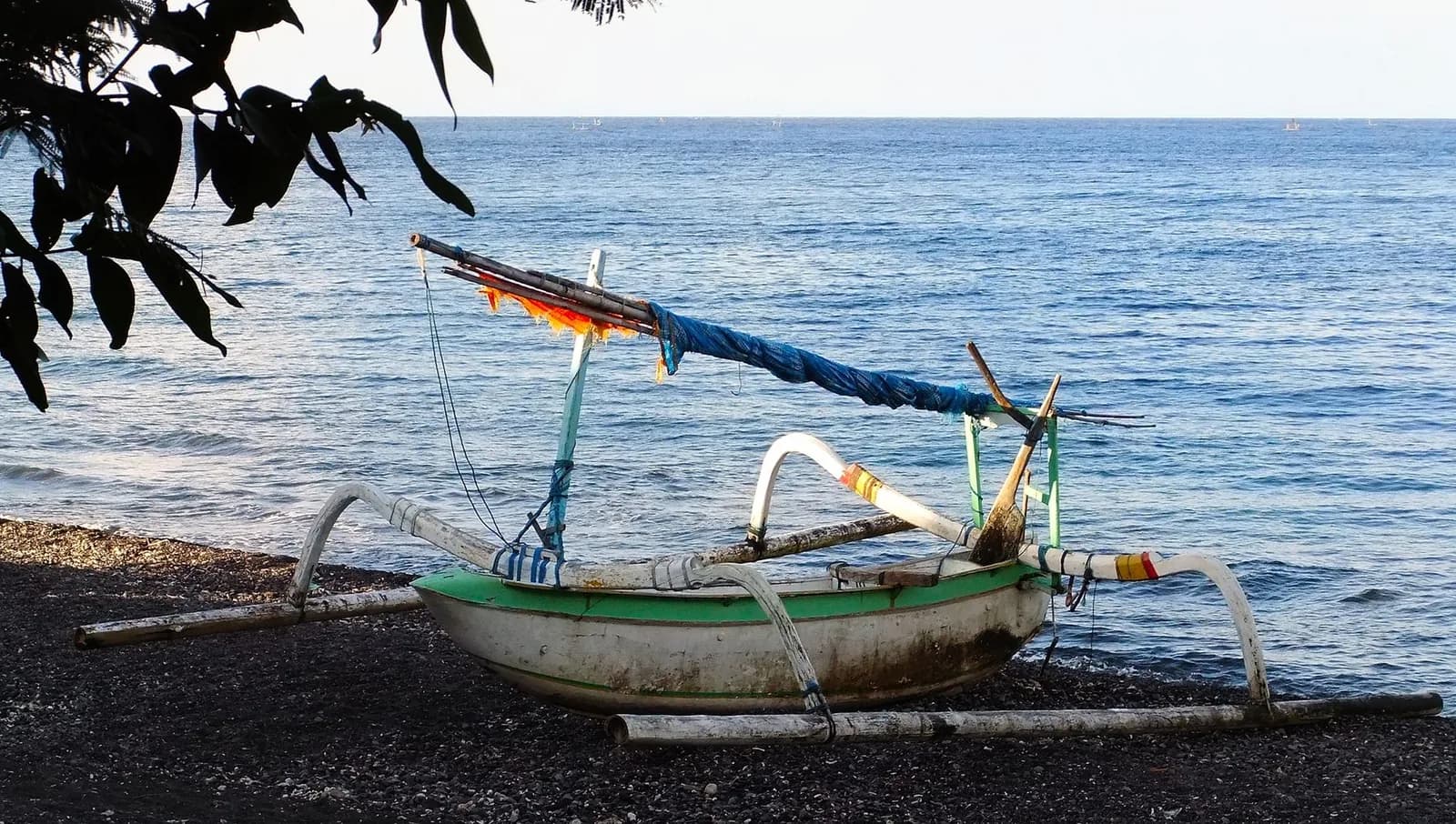 Jukung balinais échoué sur une plage de sable noir volcanique face à une mer calme, côte nord de Bali