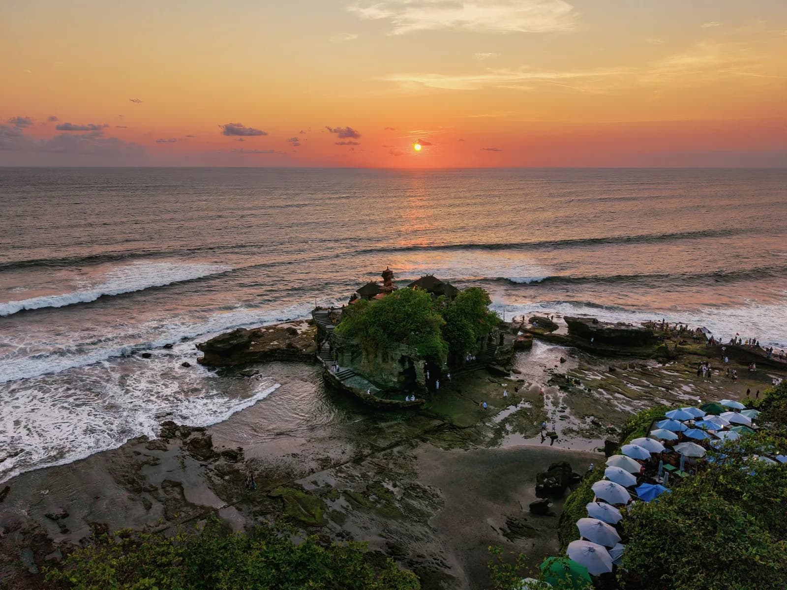 Le temple de Tanah Lot posé sur son rocher, silhouette découpée sur un coucher de soleil orange à Bali