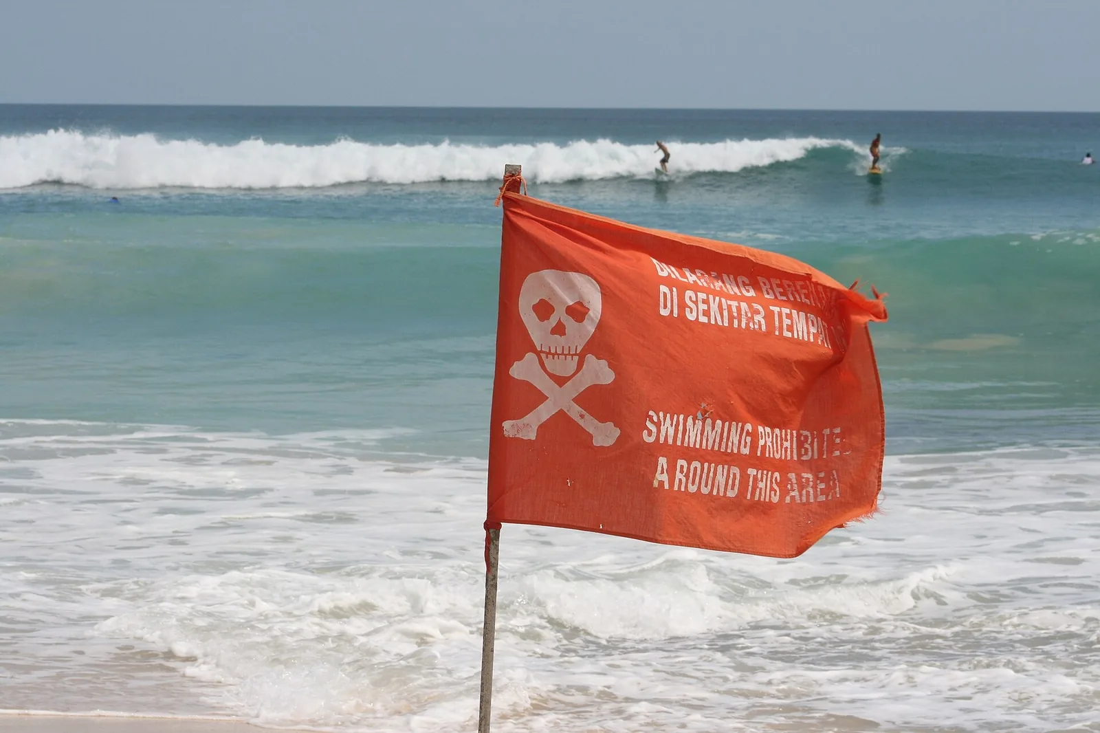 Drapeau rouge d'interdiction de baignade sur une plage de Bali, avec des surfeurs au large