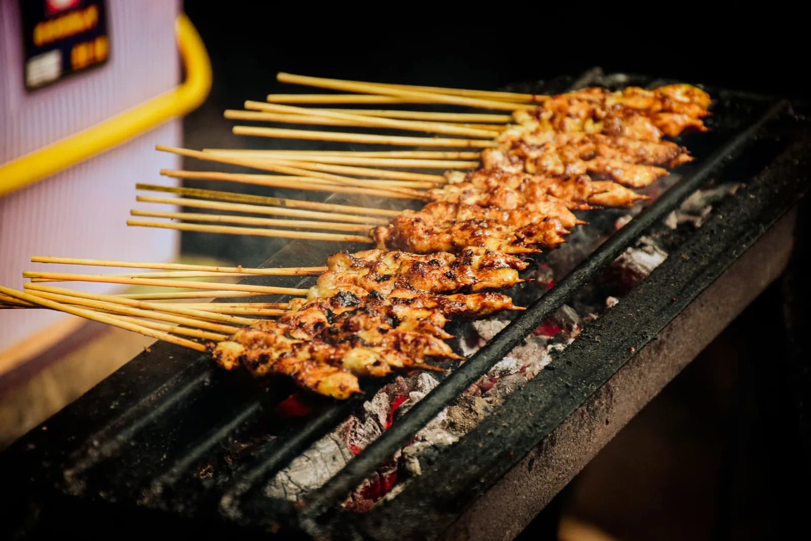 Brochettes de satay de poulet grillées sur un barbecue à braises, sur un stand de nourriture de rue
