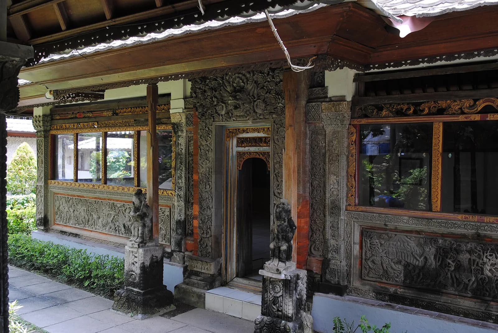 Pavillon balinais en bois et pierre aux portes et murs sculptés, gardés par des statues de pierre, au musée Le Mayeur