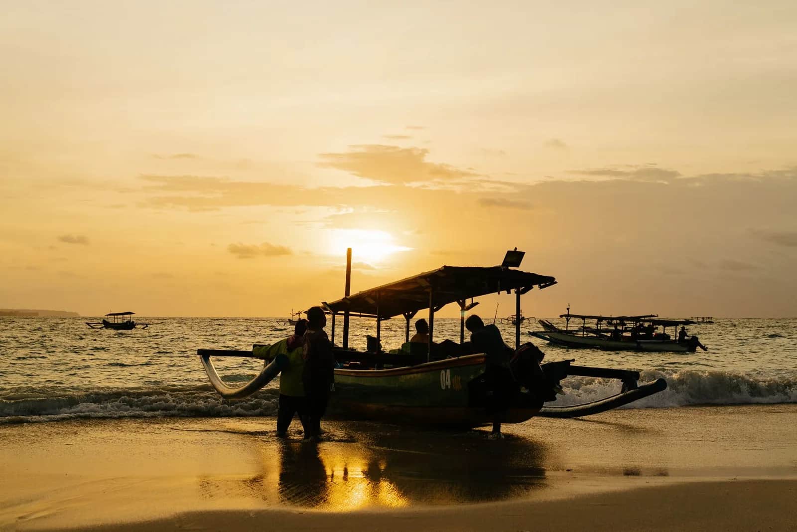 Jukung balinais, pirogue à balancier, sur le sable au lever du soleil, avec des pêcheurs en silhouette dans la lumière dorée
