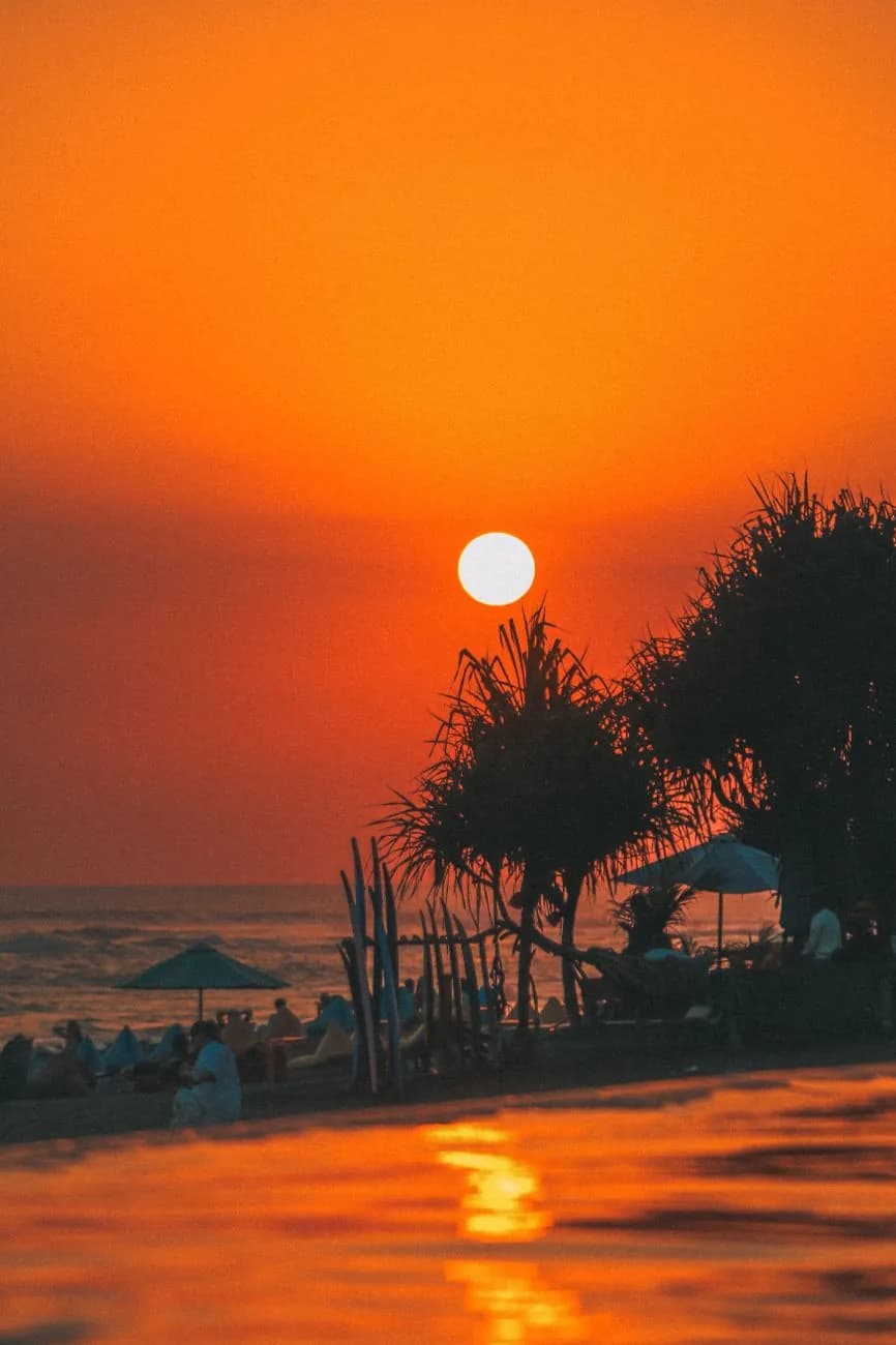 Coucher de soleil orangé sur une plage de Seminyak à Bali, parasols et beanbags d'un beach club au premier plan