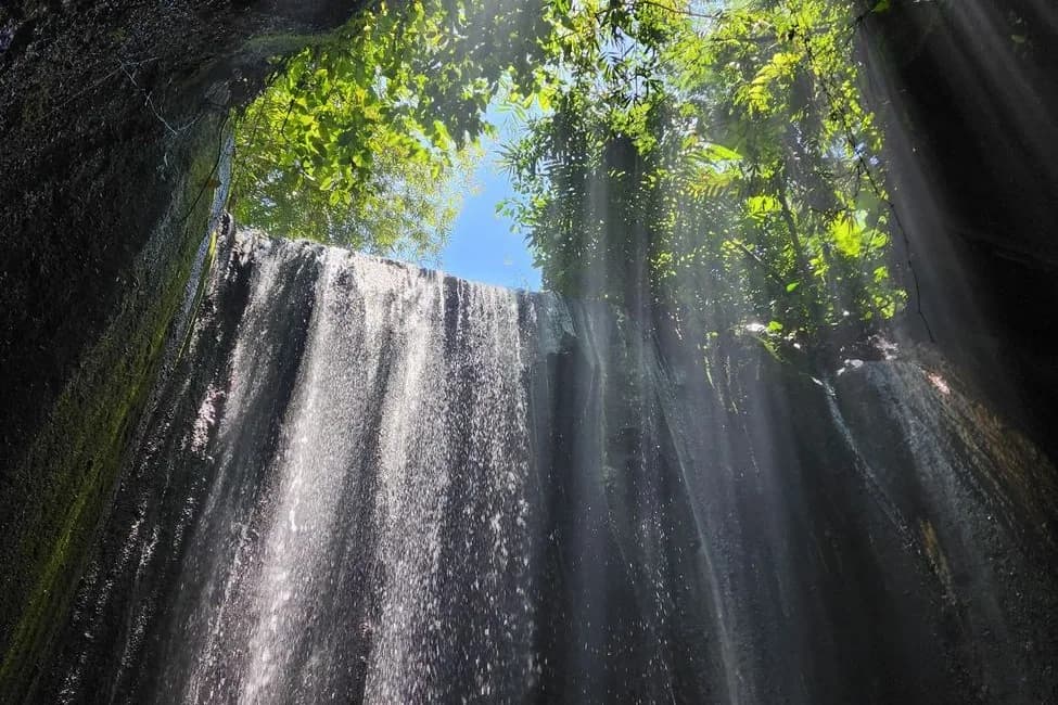 Chute d'eau de Tukad Cepung tombant dans une grotte rocheuse sous des rayons de lumière, Bali