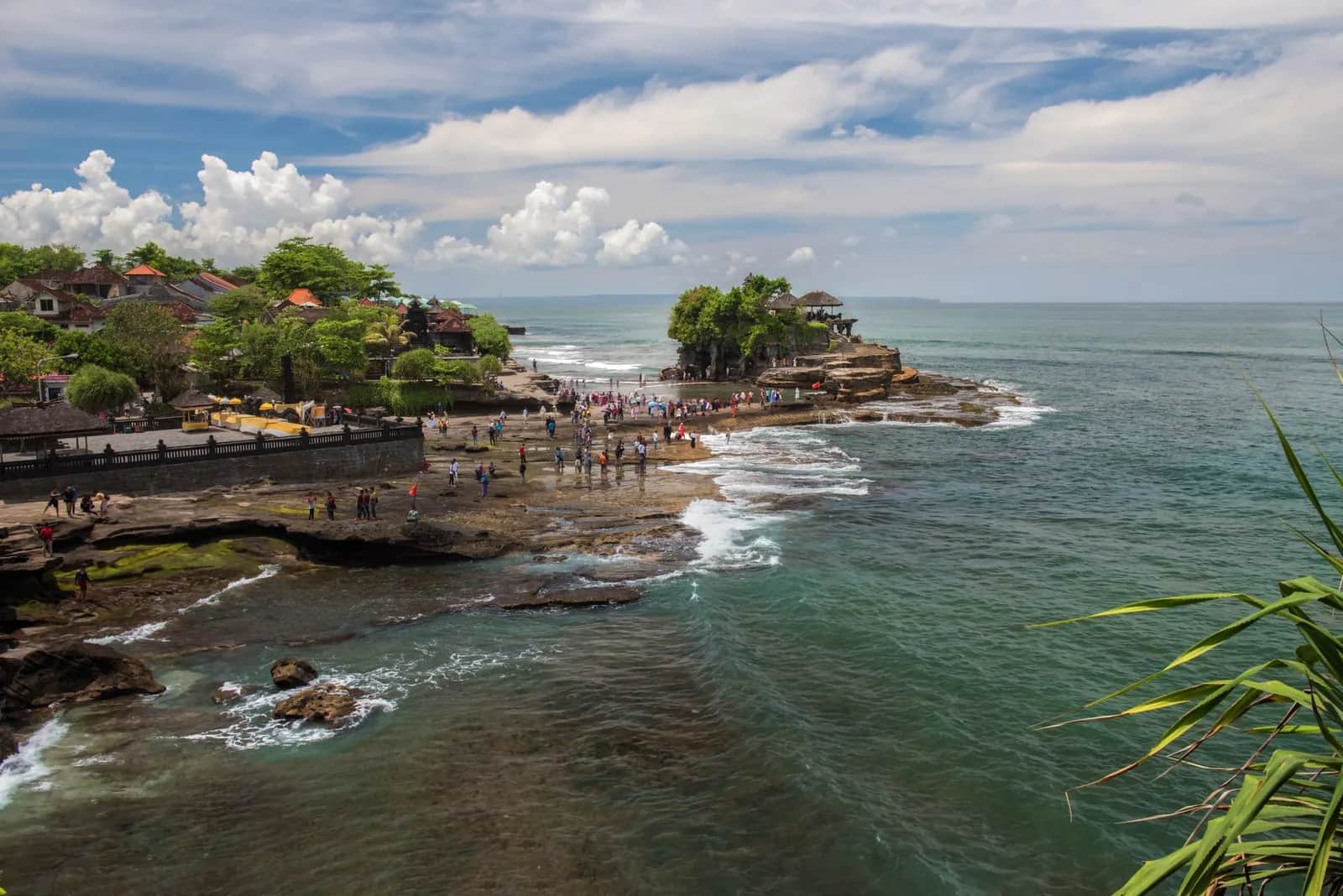 Vue large du site de Tanah Lot à marée basse, visiteurs marchant sur les rochers vers le temple, Bali