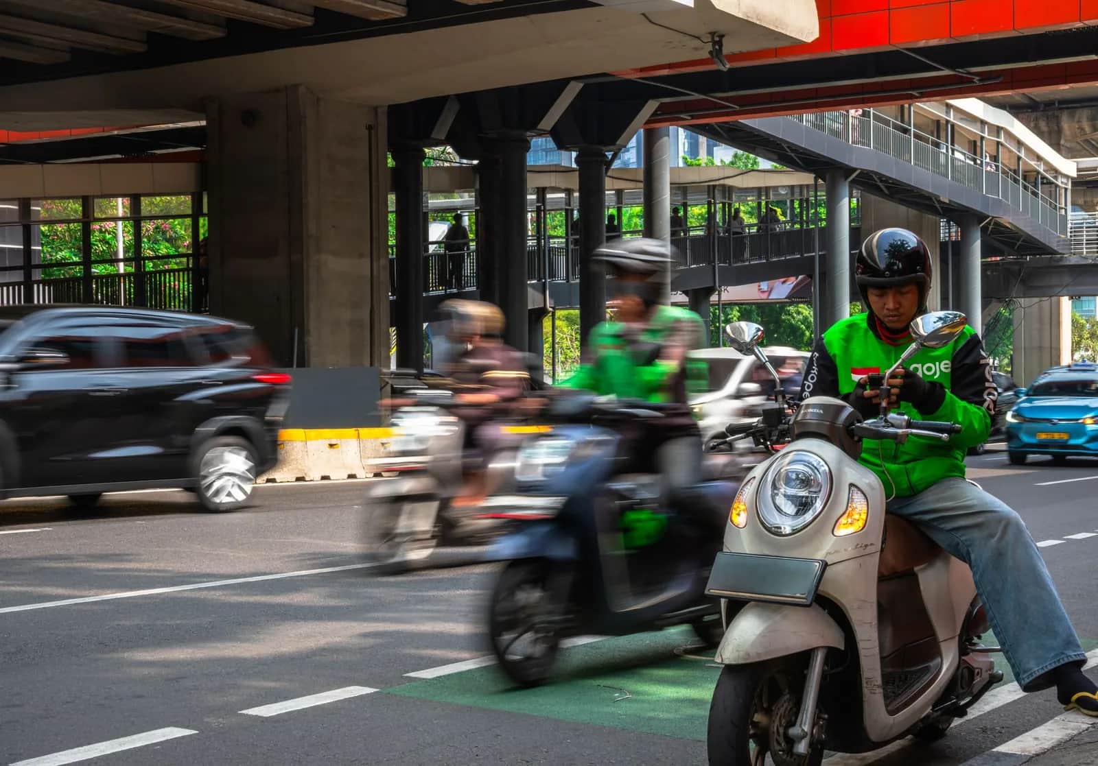 Chauffeur Gojek en blouson vert sur son scooter dans une rue de Jakarta