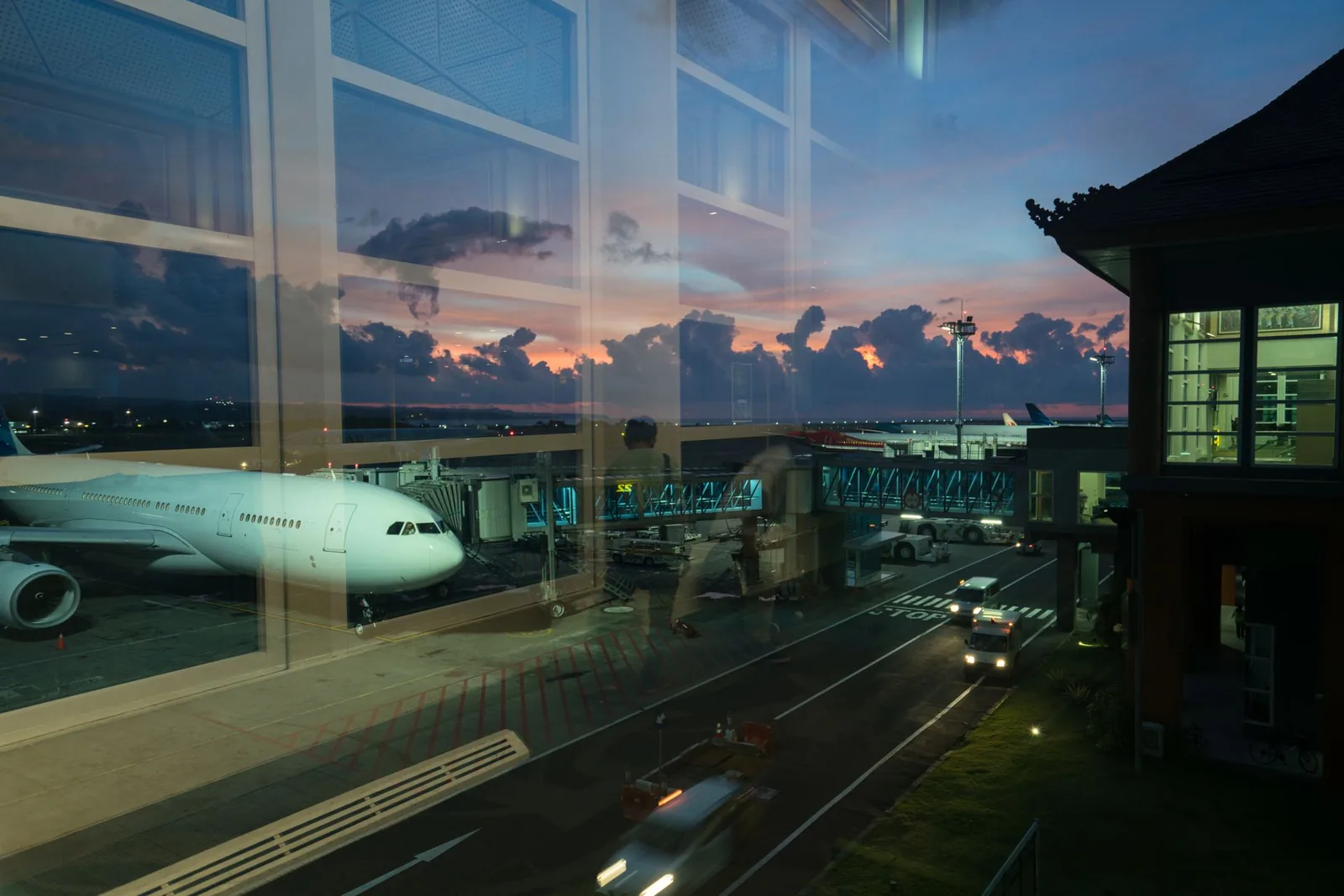 Avion à quai devant un terminal à l'architecture balinaise, au crépuscule, aéroport de Bali