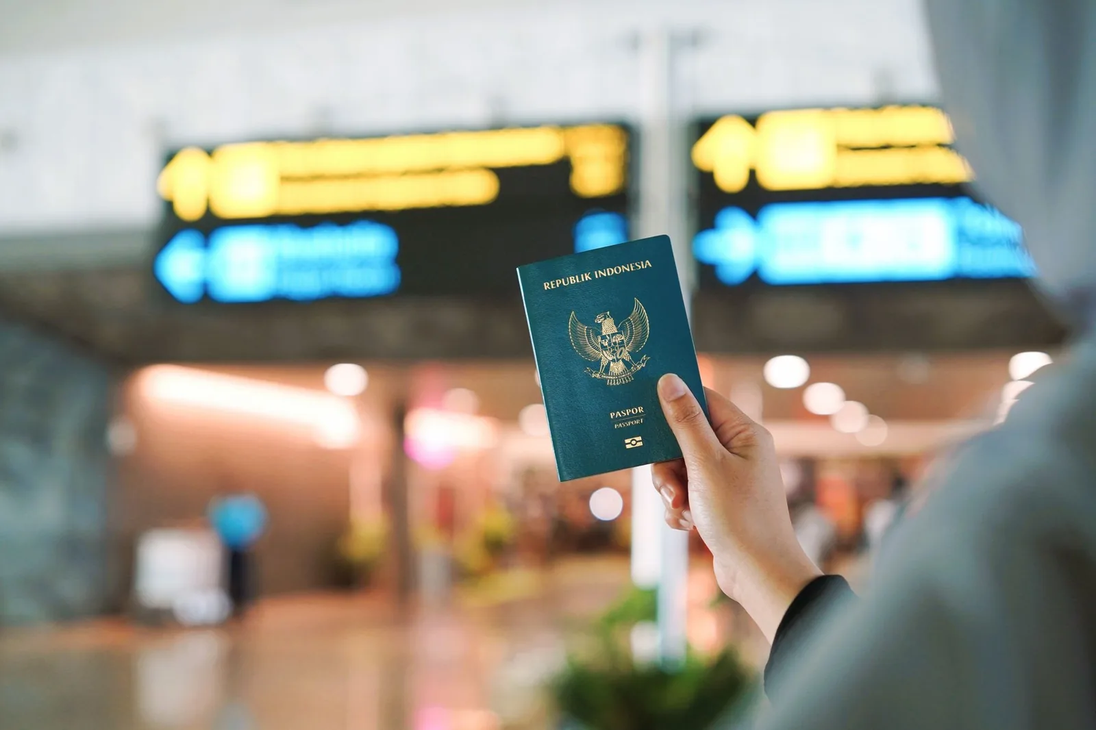 Passeport de la République d'Indonésie tenu devant les panneaux d'affichage d'un terminal d'aéroport indonésien