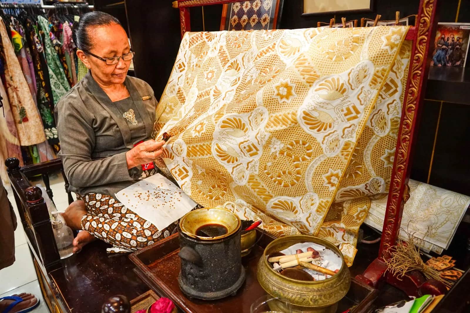 Atelier de batik à Yogyakarta : une artisane avec ses cires et un grand tissu doré tendu