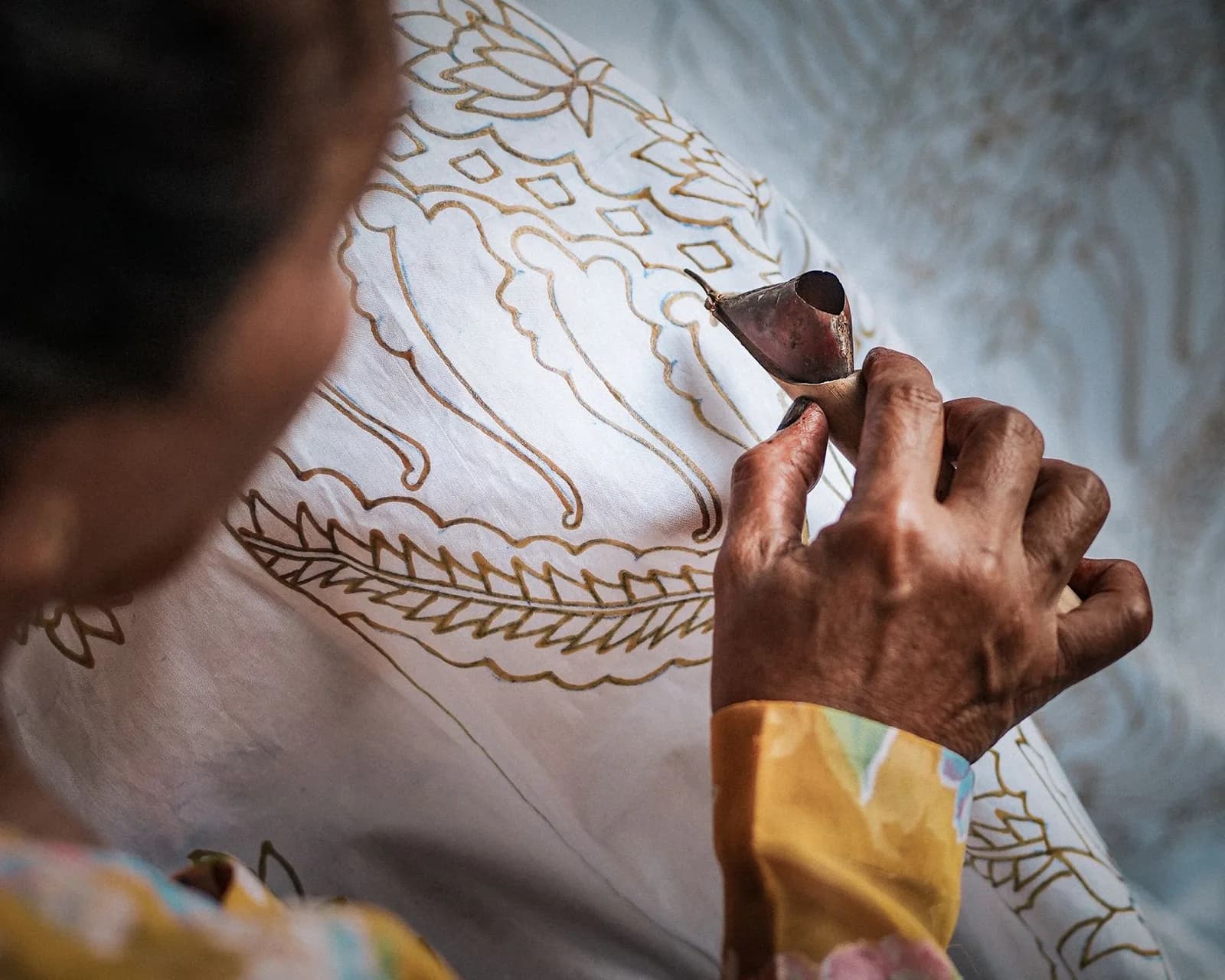 Artisane appliquant la cire au canting sur un tissu batik blanc à motifs, à Yogyakarta