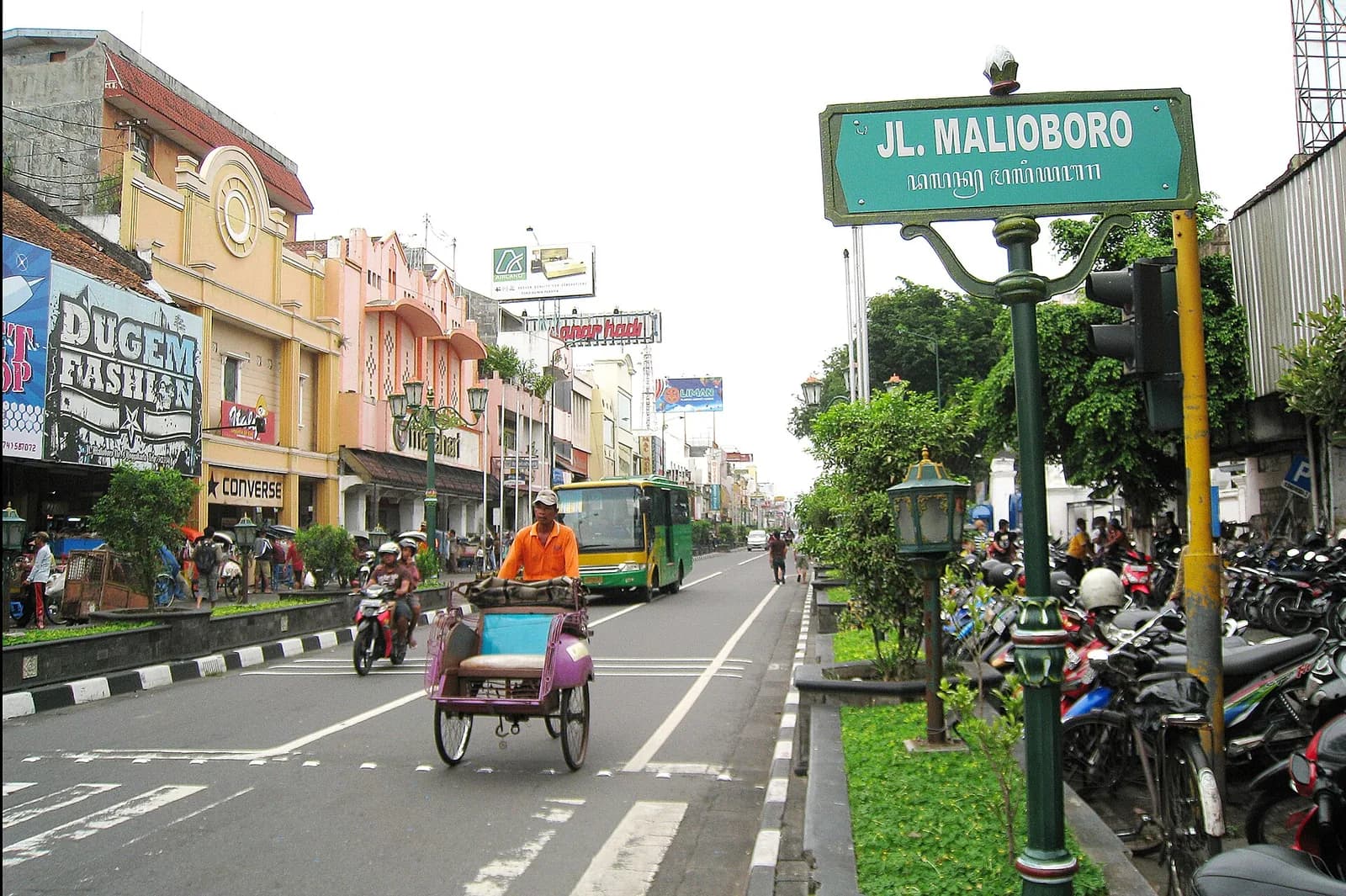 Rue Malioboro à Yogyakarta, avec son panneau vert, ses boutiques colorées, un becak et la circulation