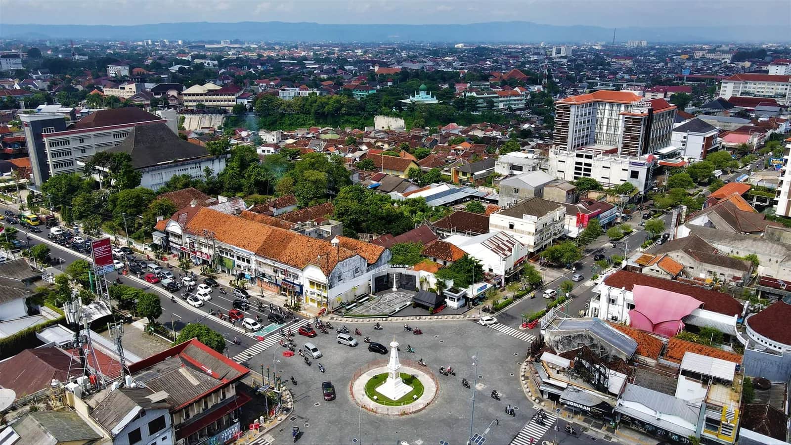 Vue aérienne du centre de Yogyakarta avec le monument Tugu au carrefour, ses toits de tuiles et les montagnes au loin